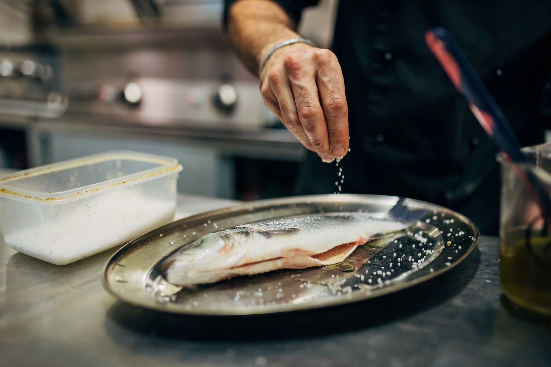 Chef seasoning a dish with a pinch of salt in a professional kitchen